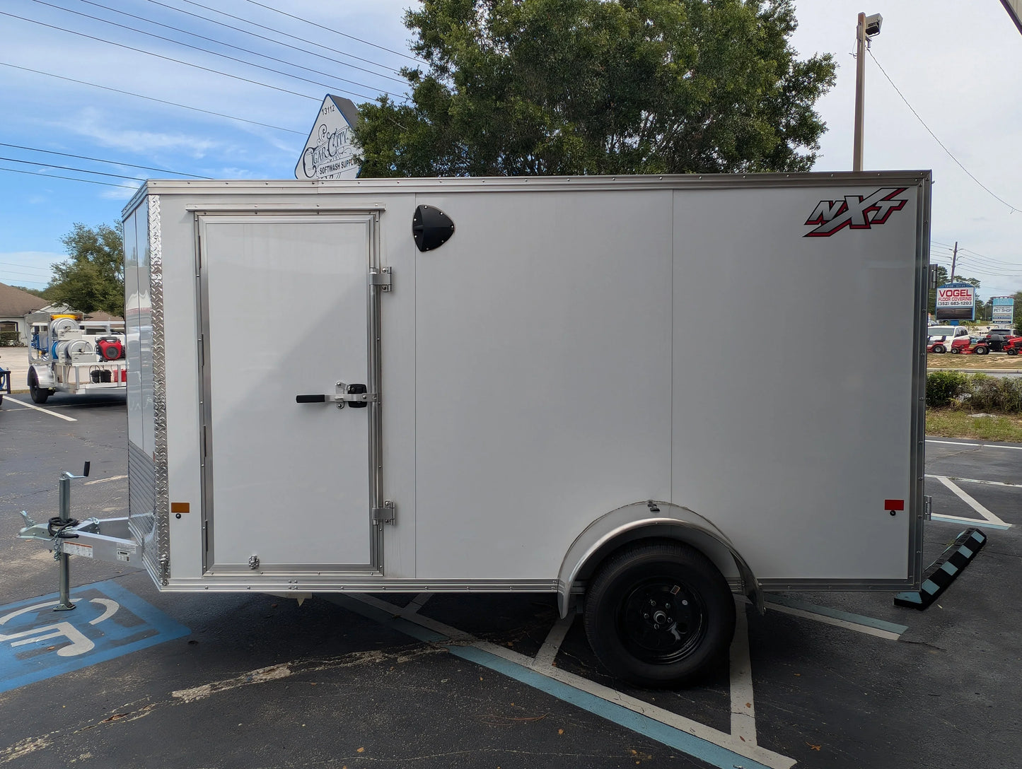 White NXT enclosed trailer for softwash equipment, parked outdoors with side door and diamond plate accents.