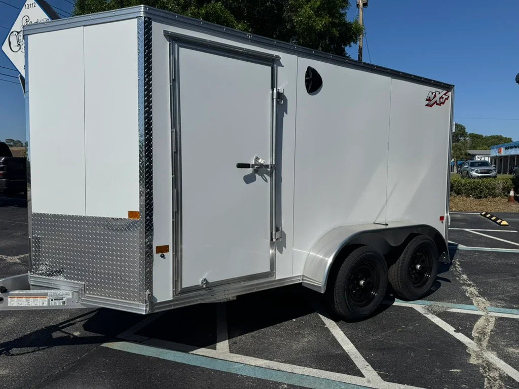 White enclosed utility trailer with rear door, diamond plate accents, and dual axles parked outdoors