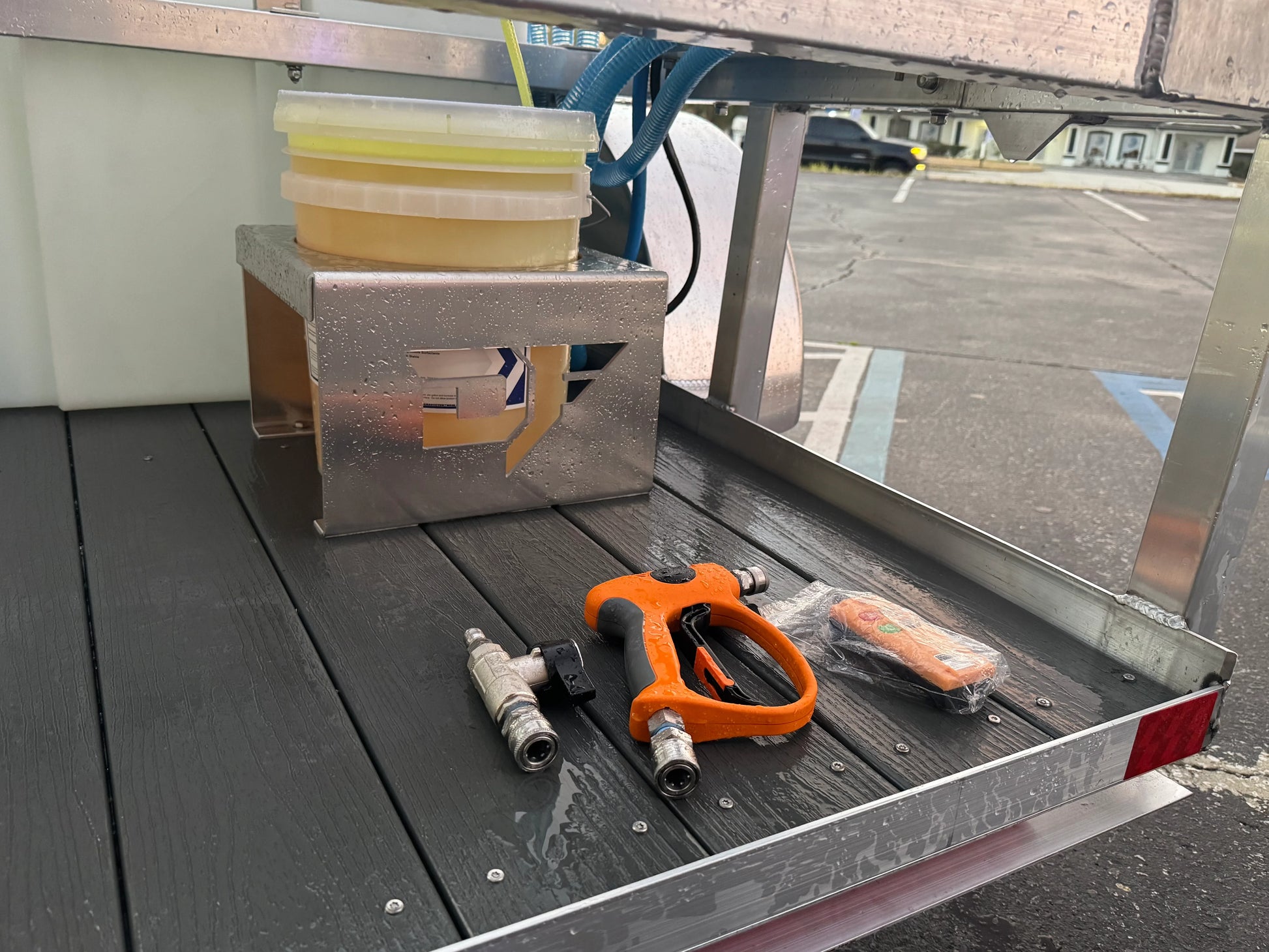 Softwash equipment setup with spray gun, hoses, and chemical containers on a wet trailer deck
