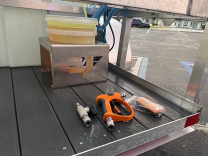 Softwash equipment setup with spray gun, hoses, and chemical containers on a wet trailer deck