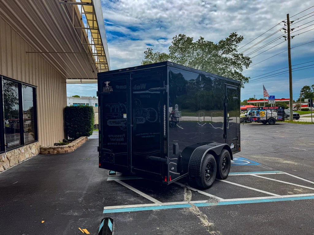 Black enclosed trailer for softwash equipment, parked outside commercial building with dual axles and rear door.
