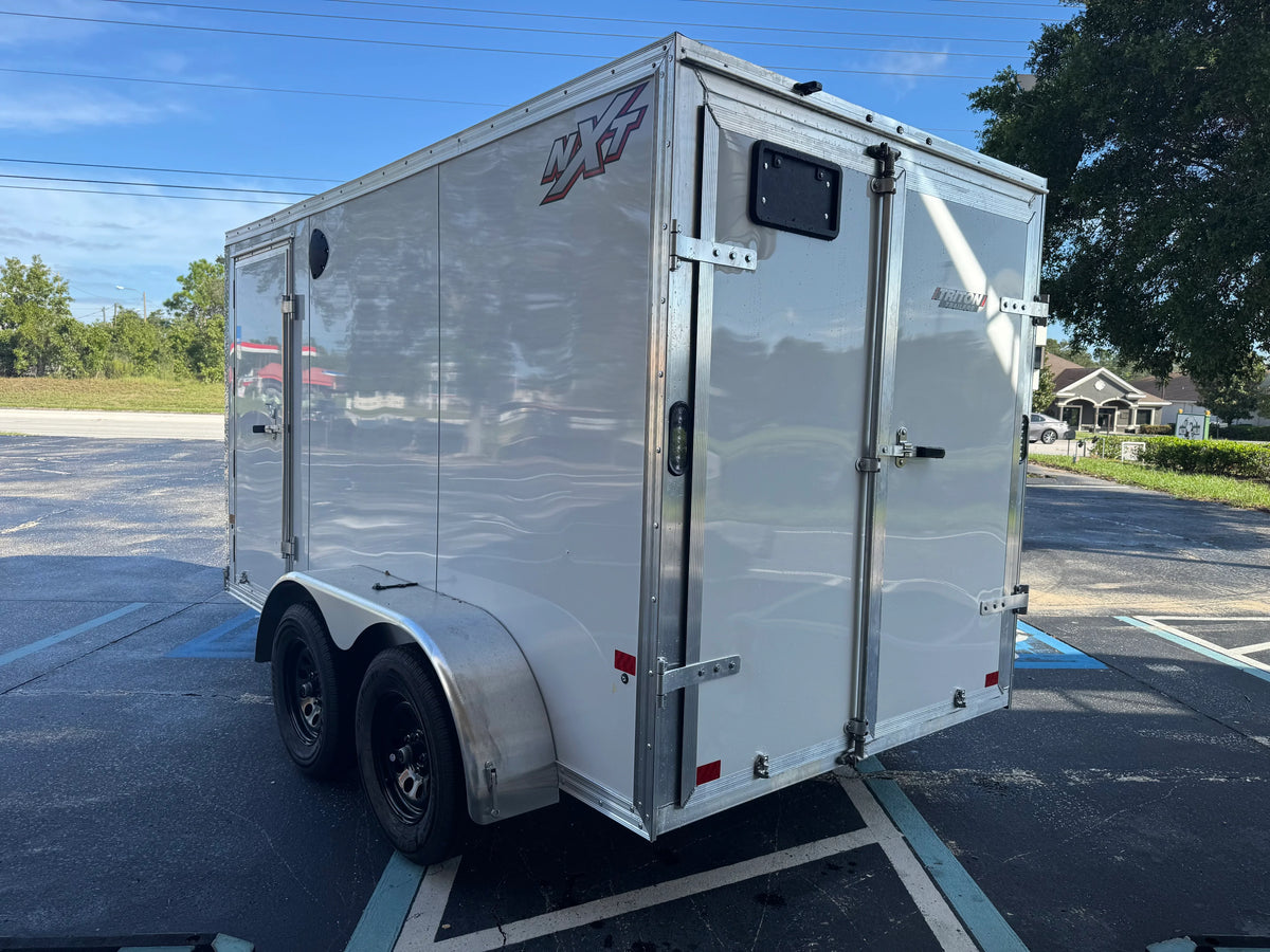 Silver enclosed trailer with NX5 branding, parked in a lot under clear skies.