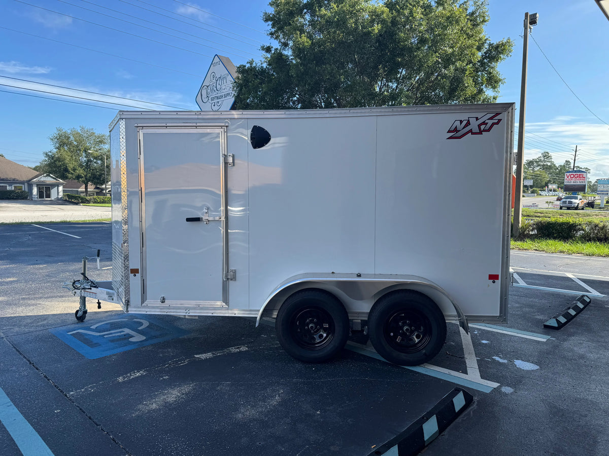 White enclosed utility trailer with NXT logo, parked in lot near softwash supply store